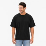 Smiling male model wearing a custom black drop shoulder oversized t-shirt by Eco Jersey, paired with light blue jeans, showcasing the relaxed fit, wide dropped shoulder, and crew neckline