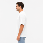 Side profile view of a male model wearing a custom white drop shoulder oversized t-shirt by Eco Jersey, paired with light blue jeans, showing the dropped shoulder seam and relaxed silhouette from the side