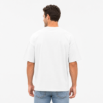 Back view of a male model wearing a custom white drop shoulder oversized t-shirt by Eco Jersey, paired with light blue jeans, showing the wide back drop shoulder construction and relaxed fit