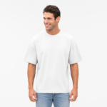 Smiling male model wearing a custom white drop shoulder oversized t-shirt by Eco Jersey, paired with light blue jeans, shown from a front angle highlighting the dropped shoulder and boxy fit