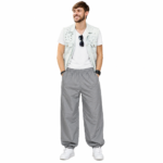 Smiling male model wearing custom gray pumper pants by Eco Jersey, styled with a white t-shirt, denim vest, and white sneakers, displaying the wide balloon fit and relaxed casual style