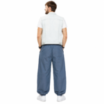 Back view of a male model wearing custom blue pumper pants by Eco Jersey, styled with a denim vest and white sneakers, showing the rear waistband, balloon leg volume, and ankle cuff detail