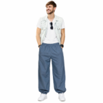 Smiling male model wearing custom blue pumper pants by Eco Jersey from the front, styled with a white t-shirt, denim vest, and white sneakers, showing the full balloon fit silhouette and elastic waistband