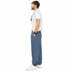 Side view of a male model wearing custom blue pumper pants by Eco Jersey, styled with a denim vest and white sneakers, showing the side profile, balloon leg, elastic waistband, and ankle cuff