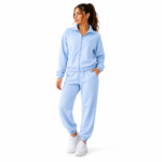 Female model wearing the super soft women's velour tracksuit in light blue colour option with zip-up mock-neck hoodie and tapered jogger sweatpants for colour reference