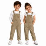 Smiling boy and girl wearing matching khaki denim overalls with white long-sleeve tops and white sneakers on a clean white background