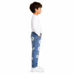 Side profile of a young boy wearing blue distressed denim jeans with all-over white daisy floral patch embroidery, white long-sleeve top, and white sneakers on a transparent background