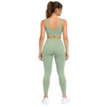 Back view of a woman wearing a light sage green sports bra and matching high-waisted leggings, with her hair in a ponytail as she looks over her shoulder.