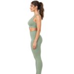 Side profile view of a woman wearing a sage green sports bra and high-waisted leggings, facing right with her hair in a ponytail.